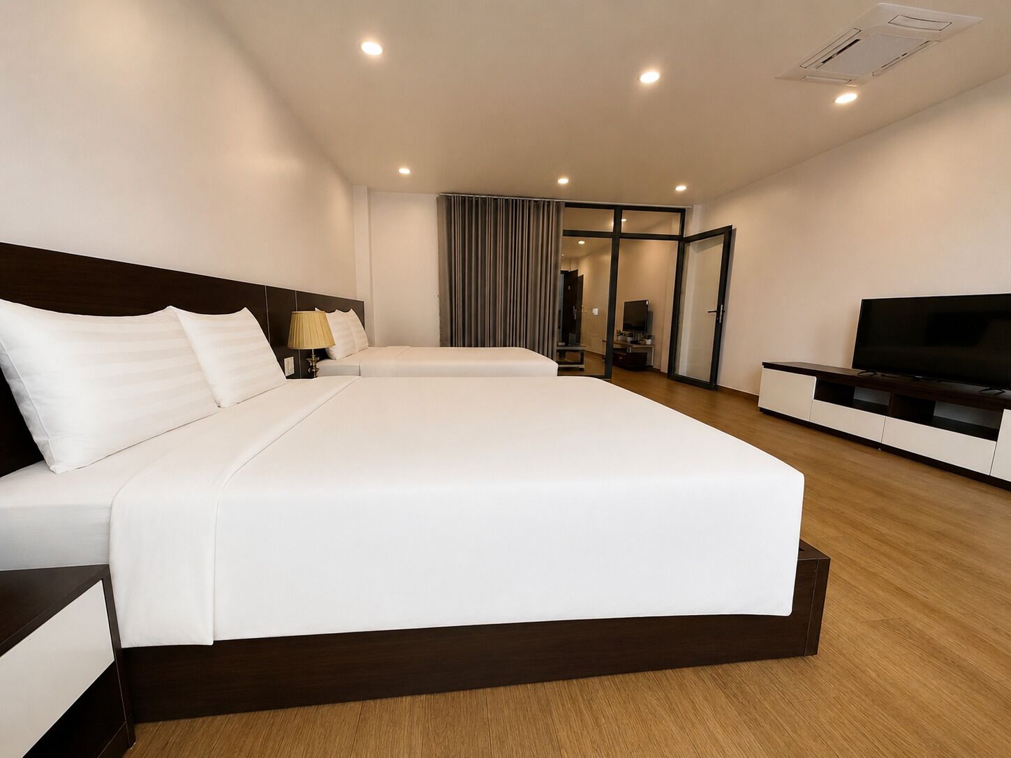 A hotel room with a large bed, a TV, and a desk with a lamp.