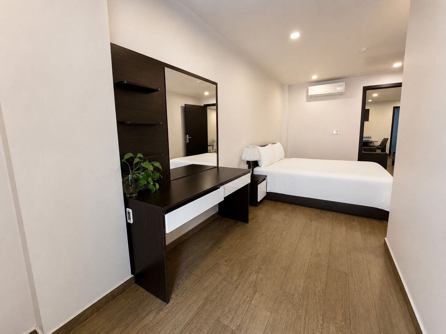 Una habitación de hotel moderna con una cama, mesita de noche, lámpara y un espejo grande.