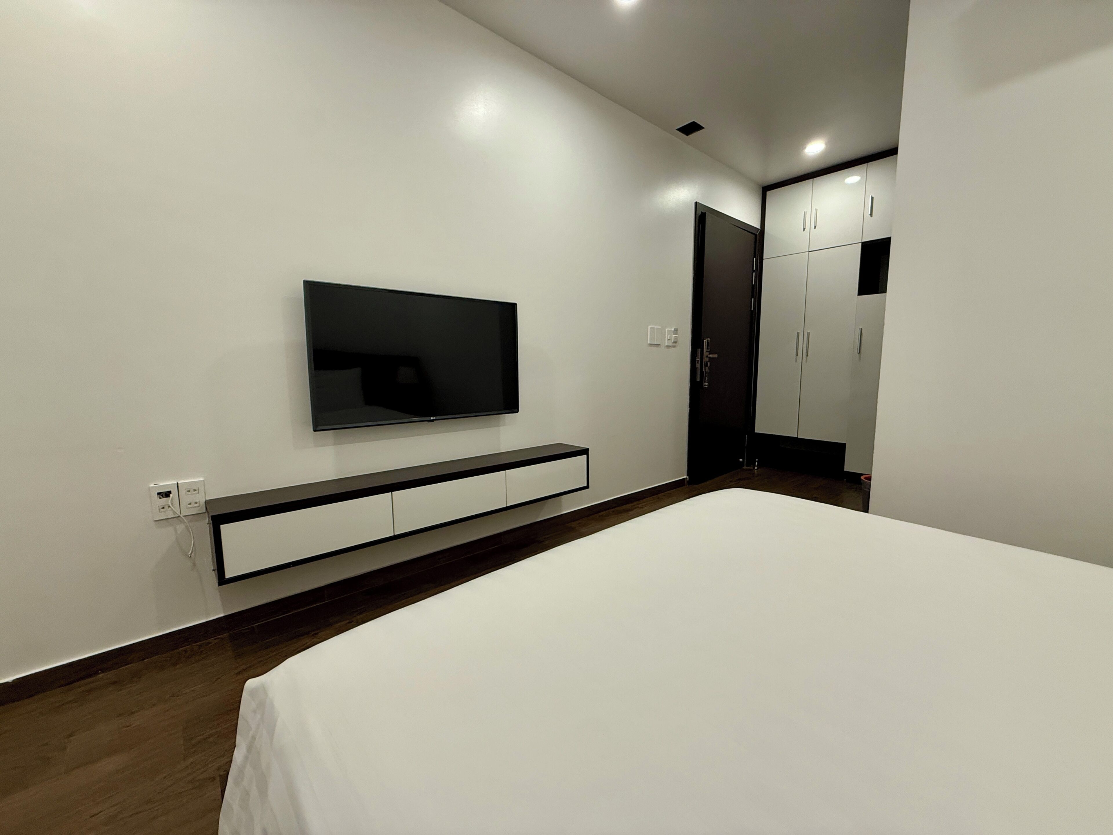 A modern bedroom with a bed, a TV mounted on the wall, and a wardrobe.
