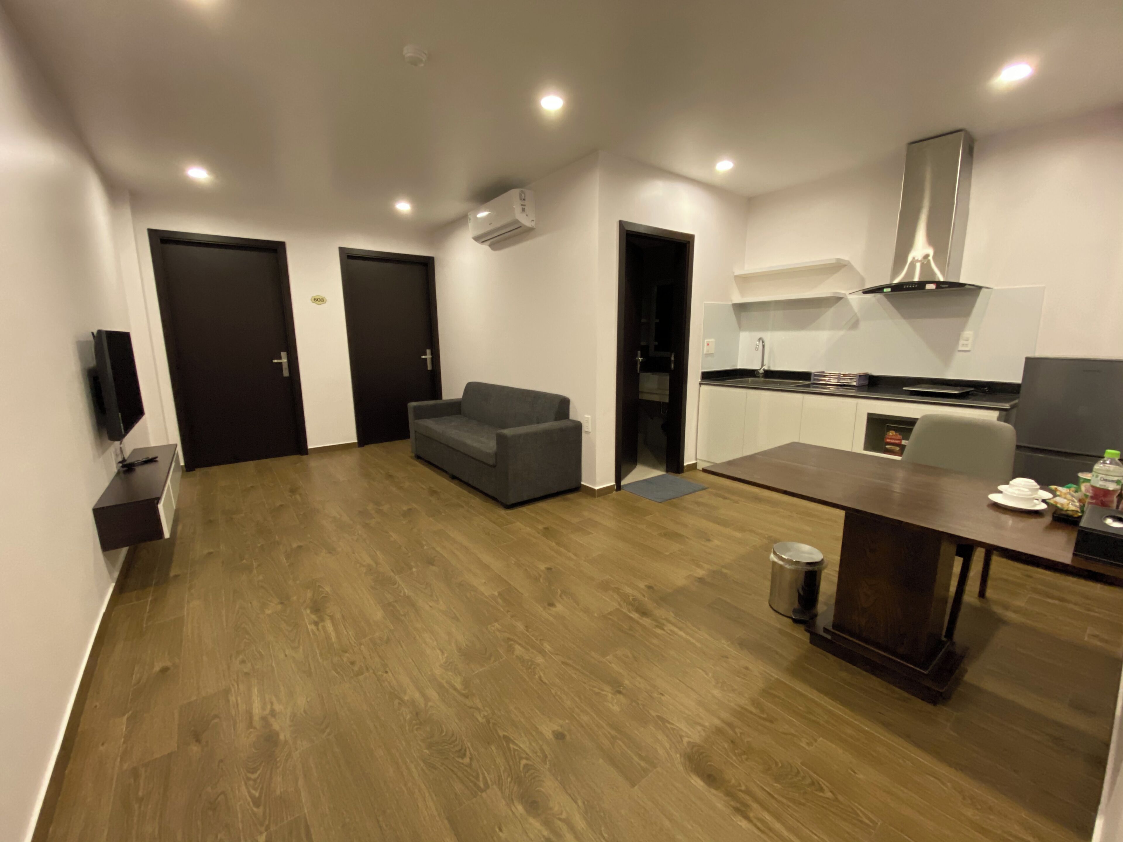 A modern apartment with a living area, a dining table, a kitchen, and a grey sofa.