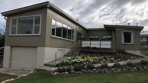 A modern two-story house with a garage, a front porch, and a landscaped garden with flowers and a stone pathway.
