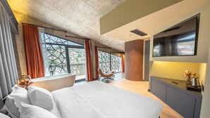 Un hotel moderno con una cama grande, un televisor montado en la pared y vistas a la ciudad a través de amplias ventanas.