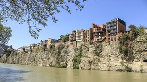 Un hotel a orillas del río con varias edificaciones, un acantilado rocoso y cielo despejado.