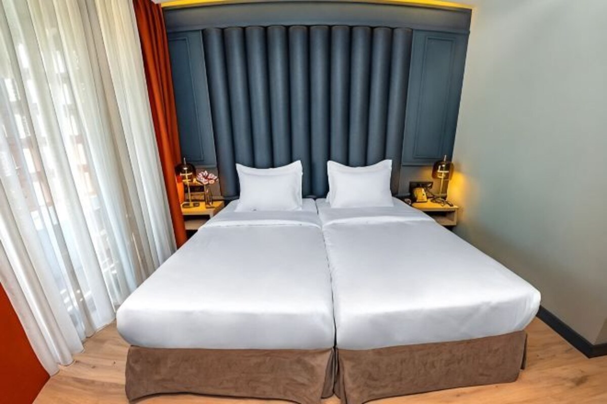 A double bed with a headboard, curtains, a nightstand with a lamp, and a wooden floor.