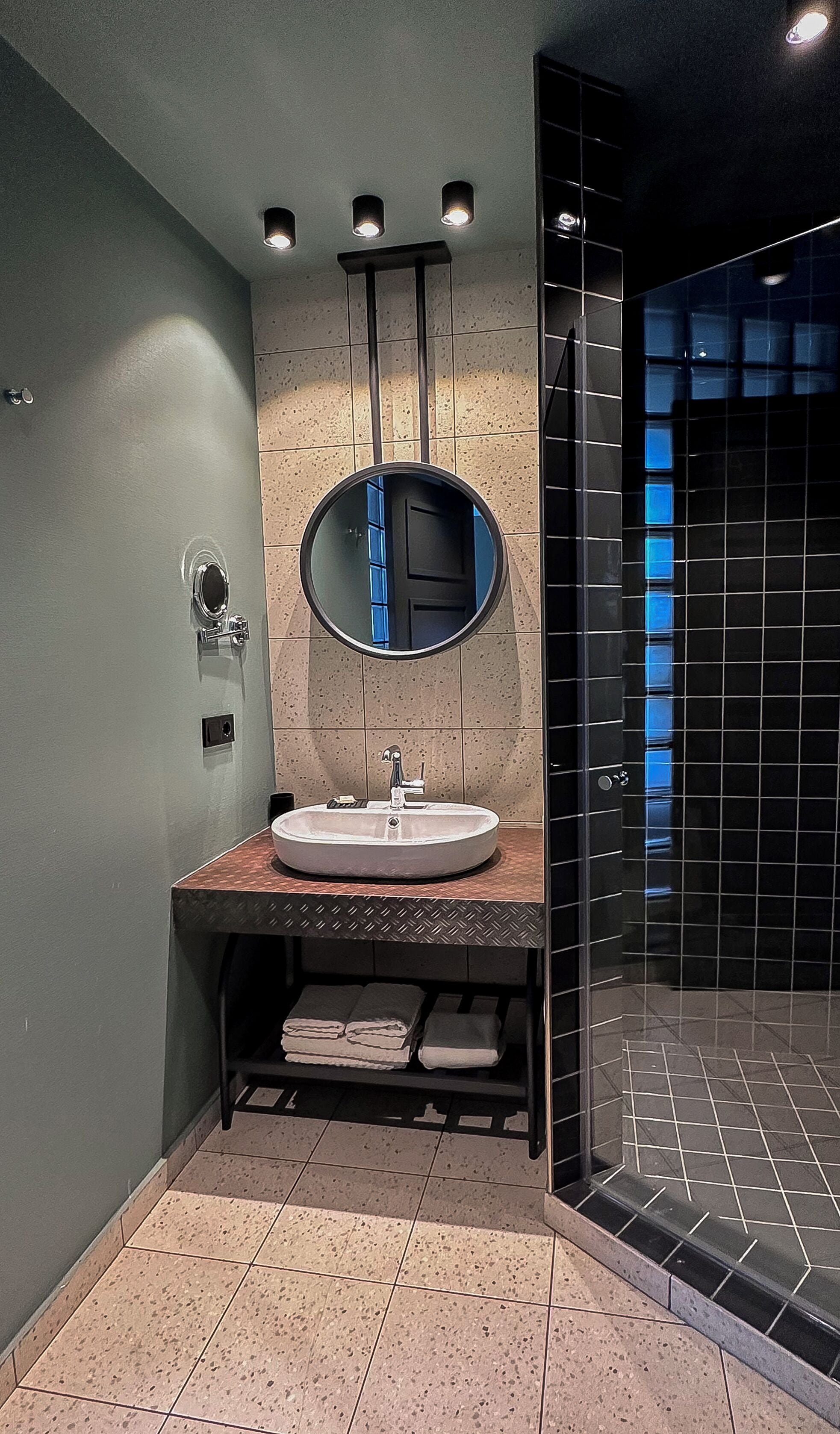 Ein modernes Badezimmer mit rundem Spiegel, Waschbecken und Duschbereich.