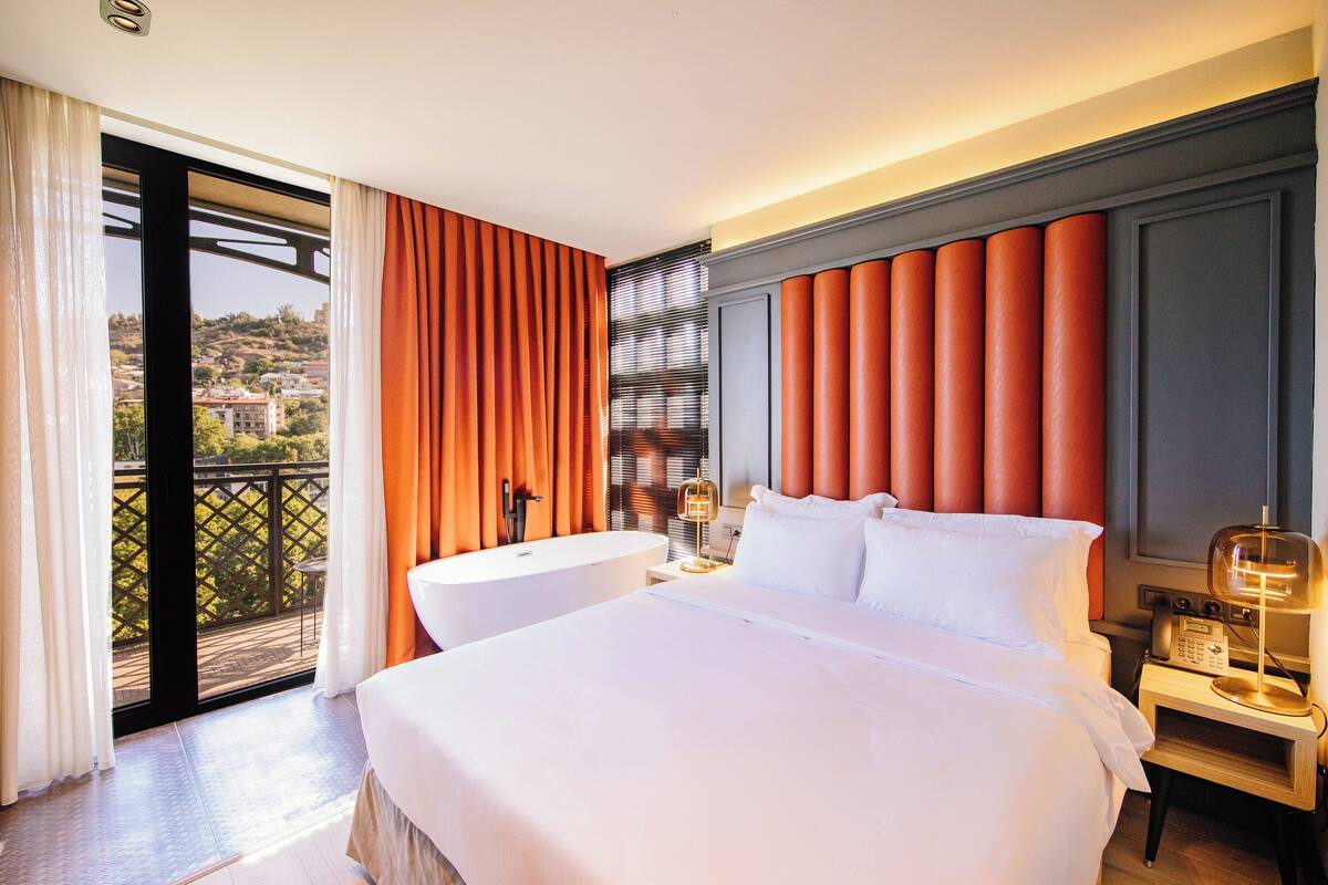 A hotel room with a large bed, a separate bathroom, and a balcony with a view.