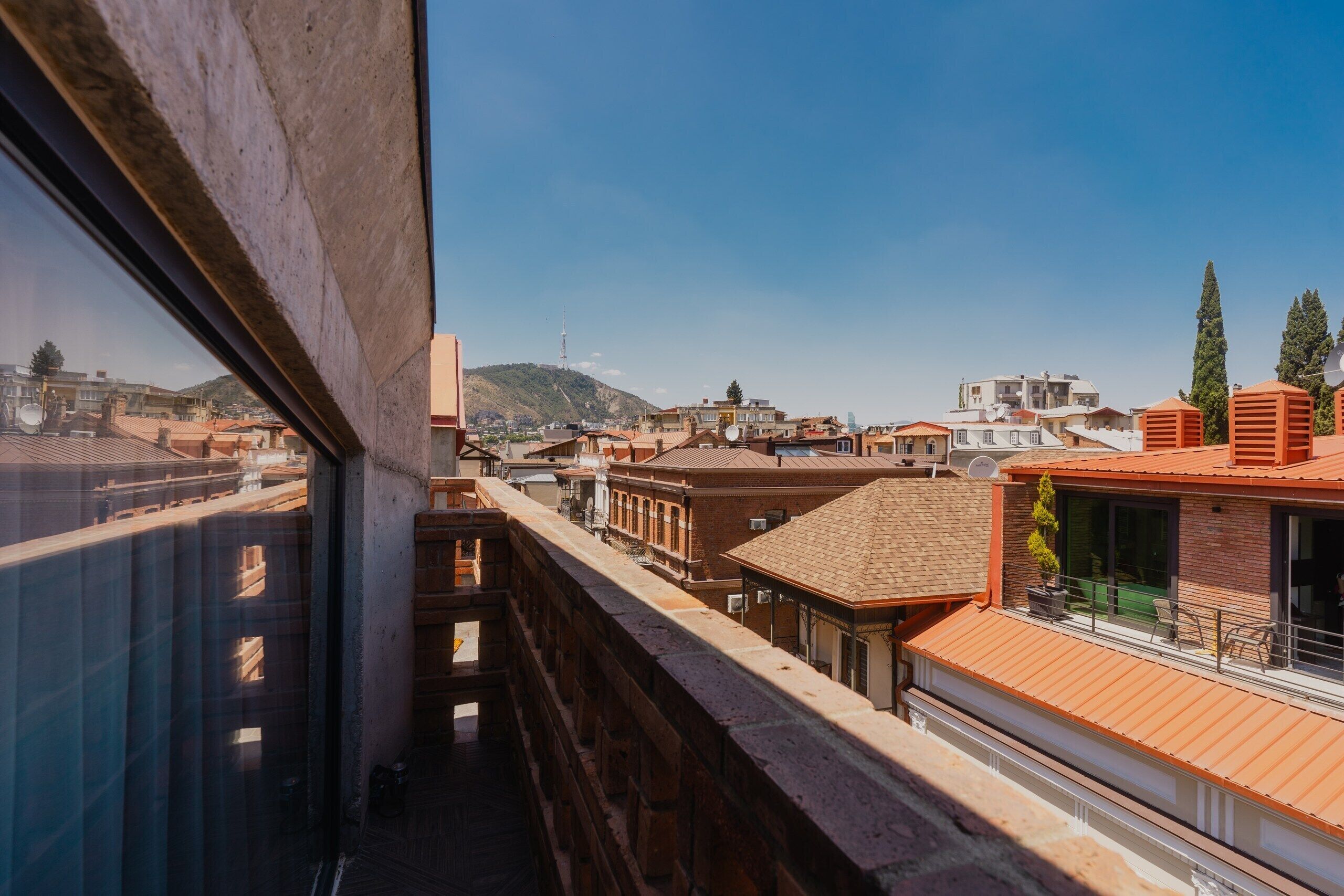 A view from a balcony overlooking a cityscape with buildings, a hill, and a clear sky.