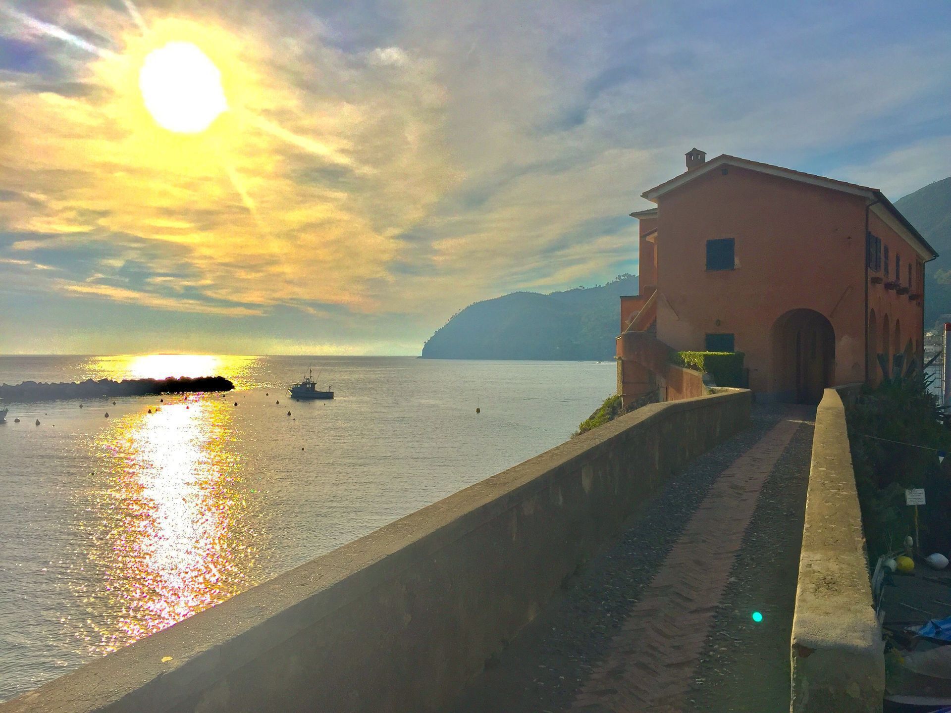 Escena costera con un edificio al lado de un paseo pavimentado que lleva al mar.