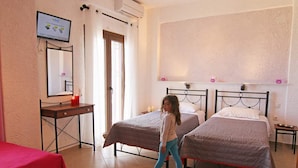 A bedroom with two beds, a desk, and a TV on the wall. - Anemi Apartments (Ikaria)