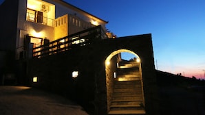 A two-story building with a staircase leading to a balcony. - Anemi Apartments (Ikaria)