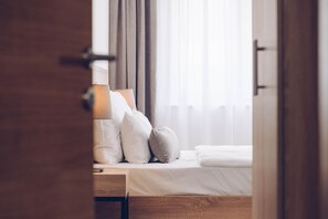 A hotel room with a bed, pillows, a nightstand, and a window with curtains.
