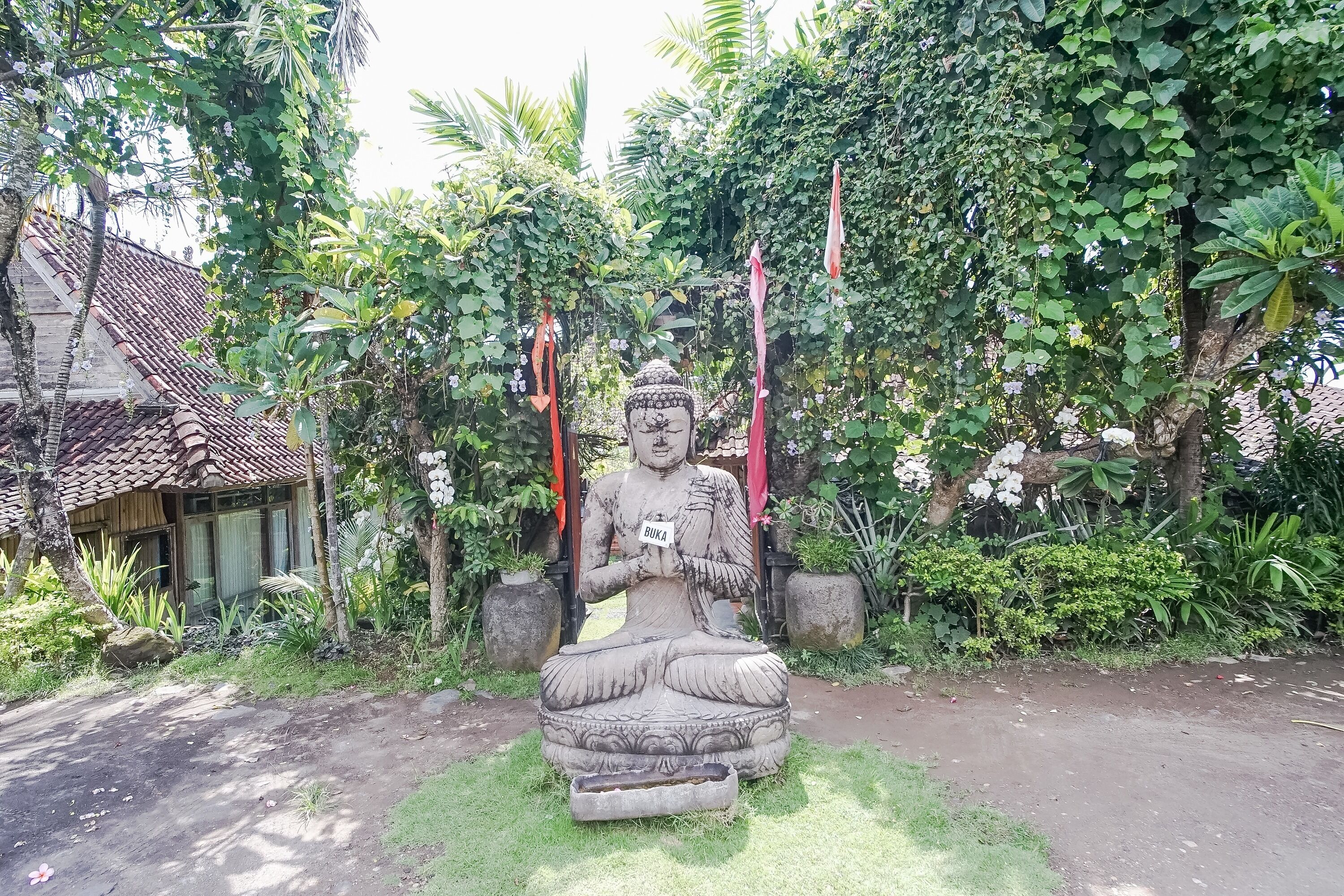 A large outdoor statue of a seated figure in a natural setting with a house in the background.