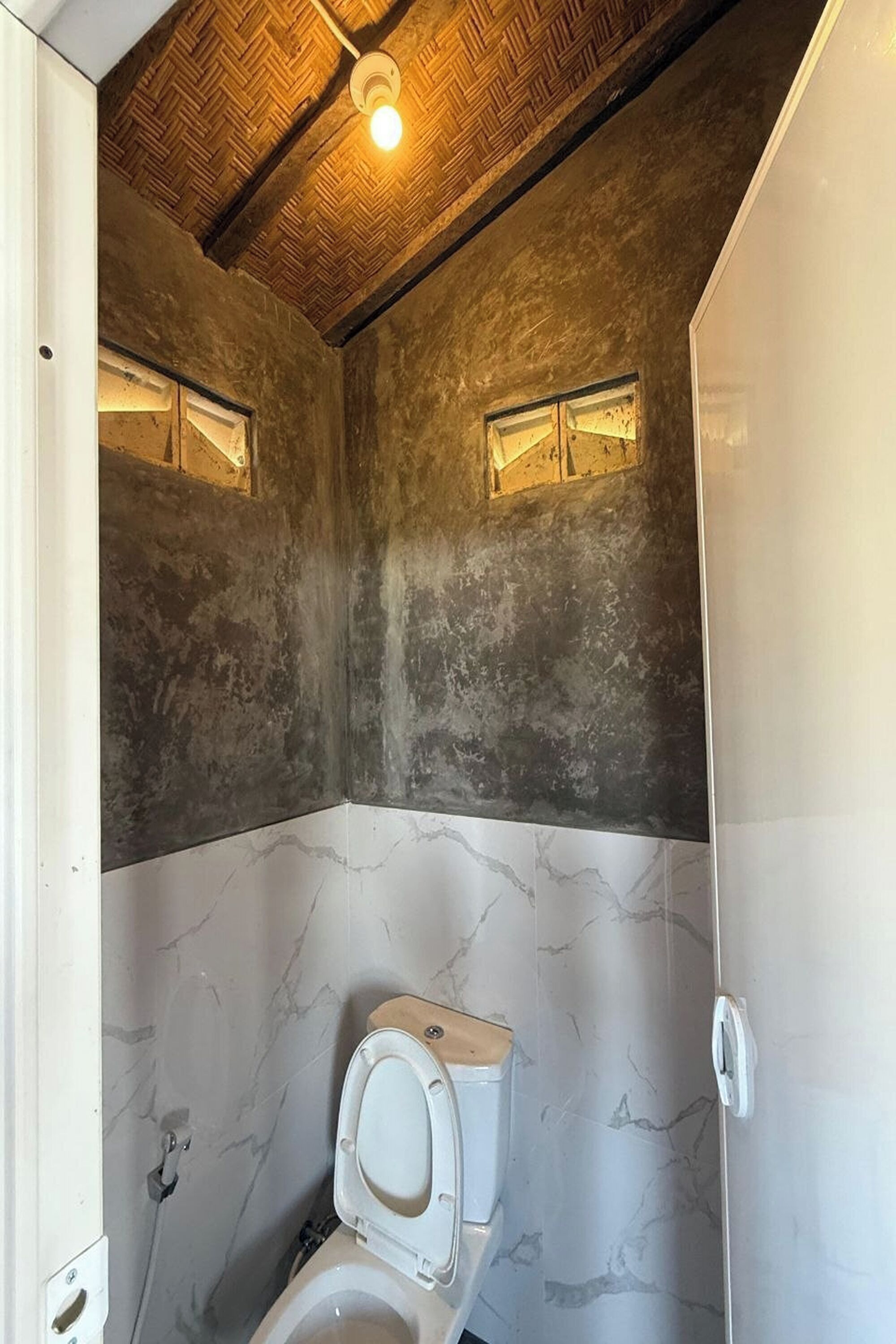 A bathroom with a wooden ceiling, a toilet, and a marble wall.