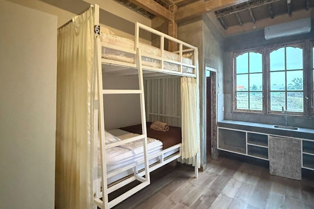 A bunk bed with a curtain, a window with a view, and a wooden ceiling.