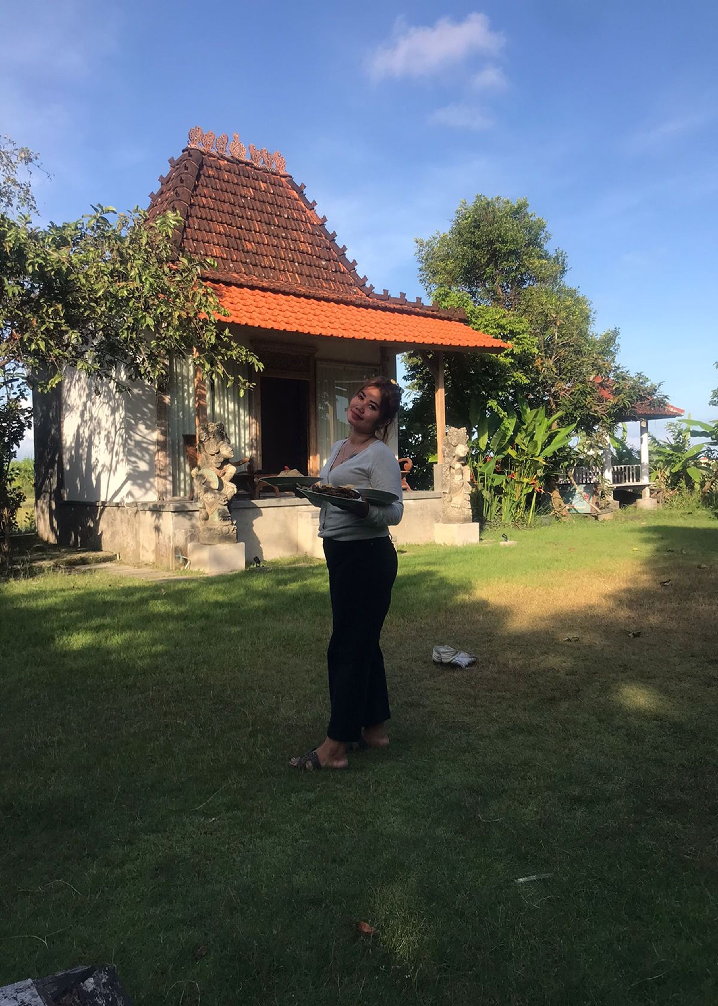 A person standing in a grassy area with a traditional building featuring a tiled roof in the background.