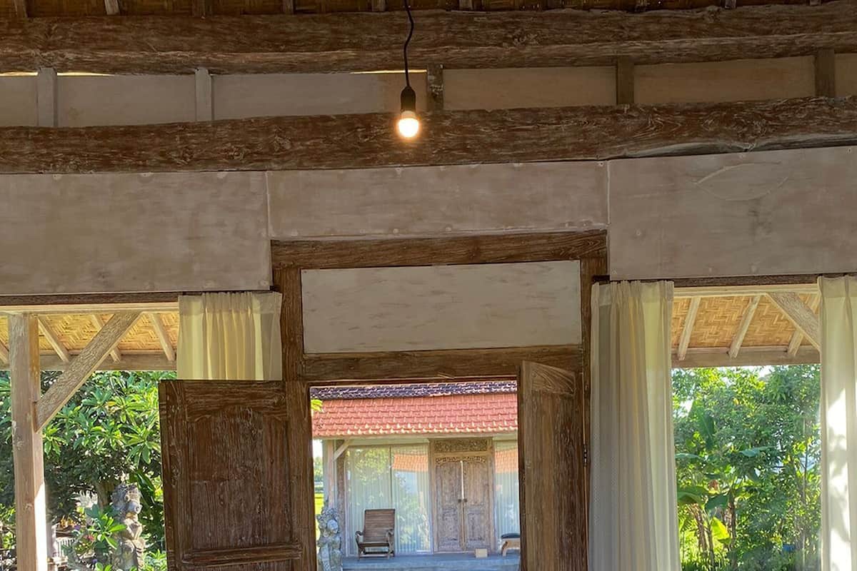 A room with a bed, a wooden door leading to an outdoor area, and a view of a building with a red roof.