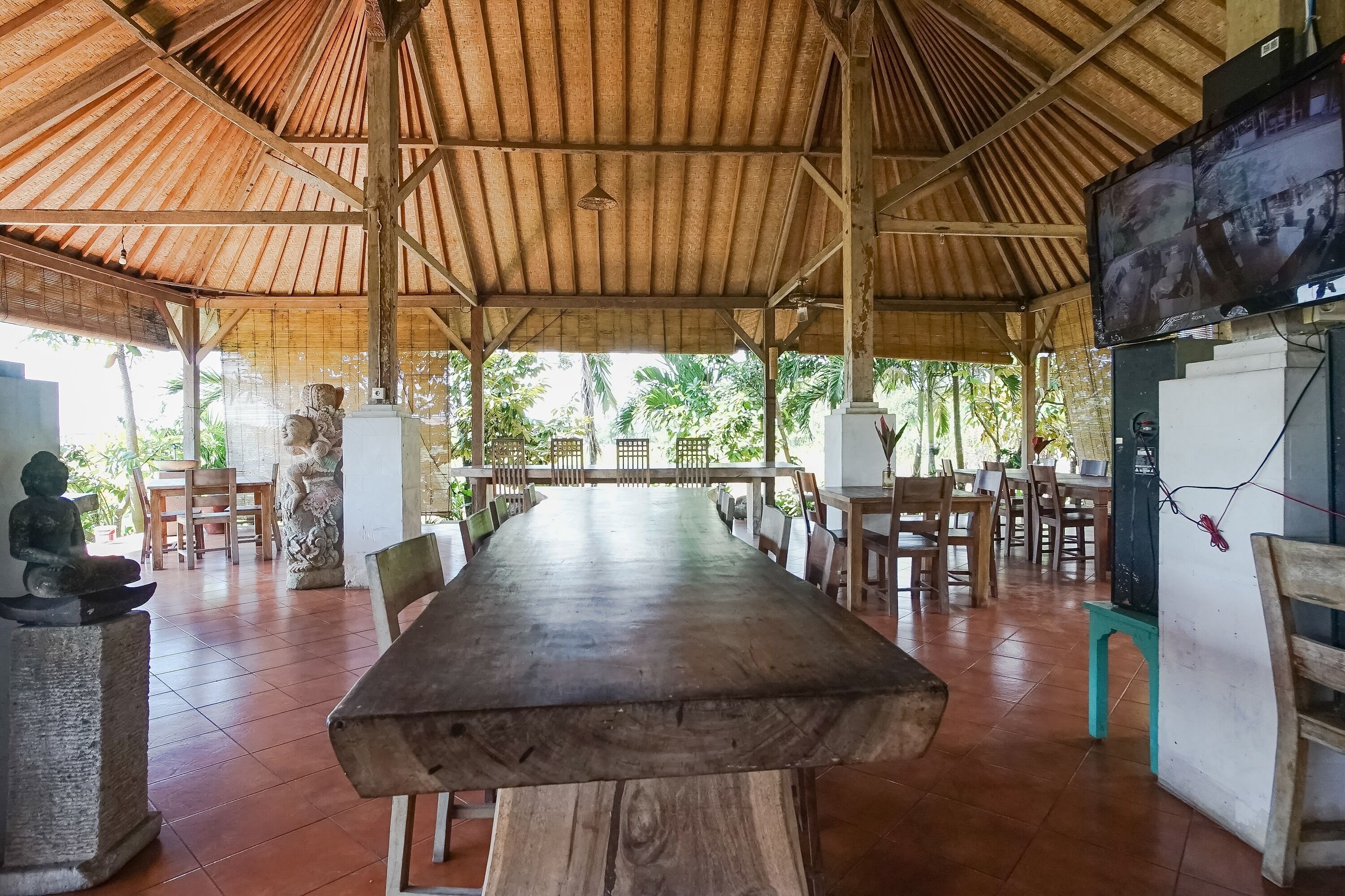A covered outdoor dining area with a long wooden table, chairs, and stone sculptures.