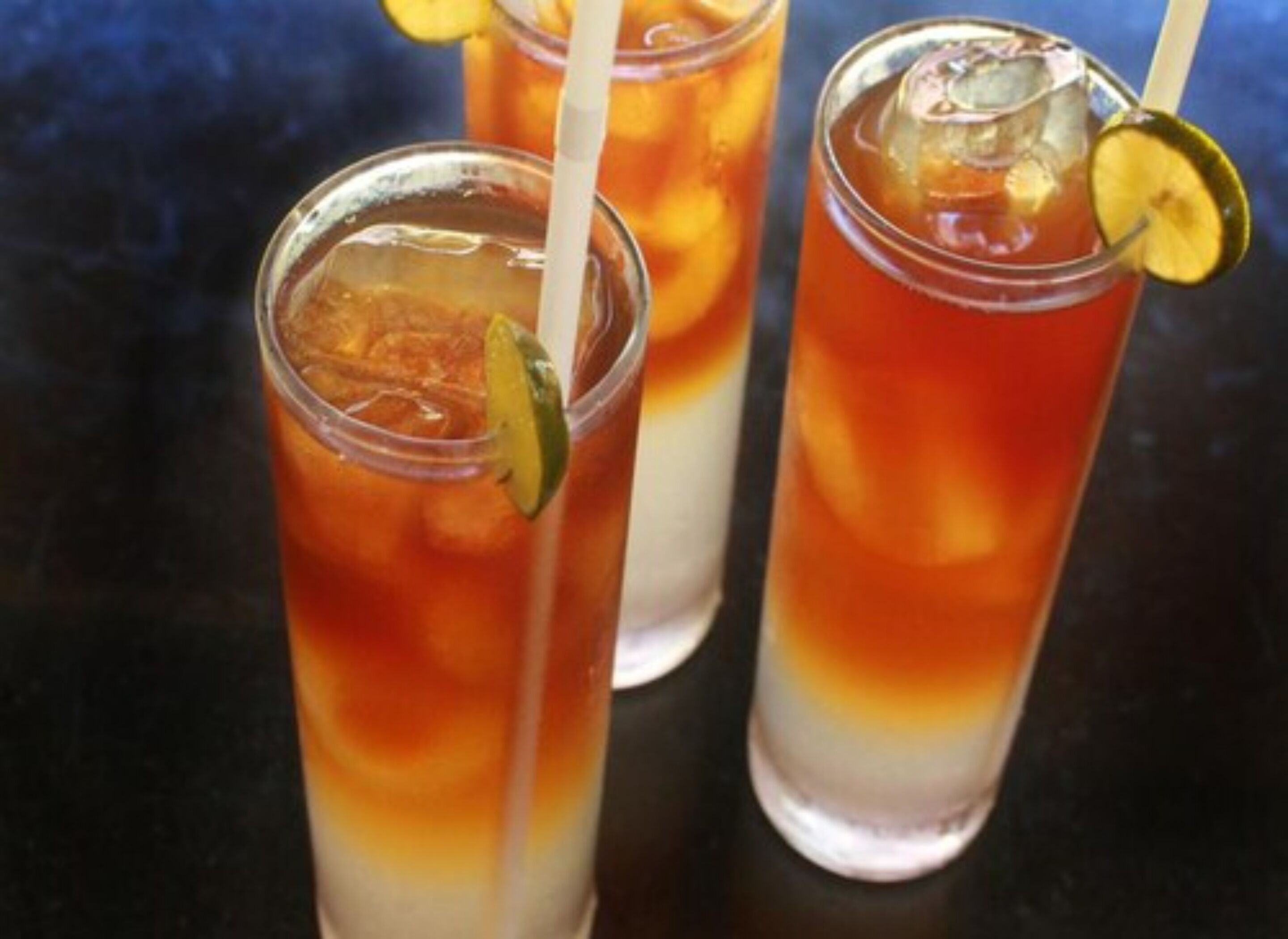 Tres vasos altos de té helado con rodajas de limón y pajitas.