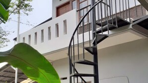 A residential building with a spiral staircase, a covered porch, and a large green leaf in the foreground. - Nabila Syar'i Guesthouse (Ngamprah)
