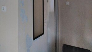 A room with peeling paint on the walls, a door, and a light switch. - Nabila Syar'i Guesthouse (Ngamprah)