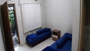 A small, clean room with two blue beds, a white curtain, a small wooden nightstand, and a door leading outside. - Nabila Syar'i Guesthouse (Ngamprah)