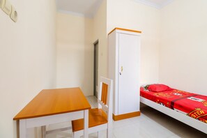 Una habitación pequeña con una mesa de madera, una silla blanca, un armario blanco y una cama individual con colcha roja.