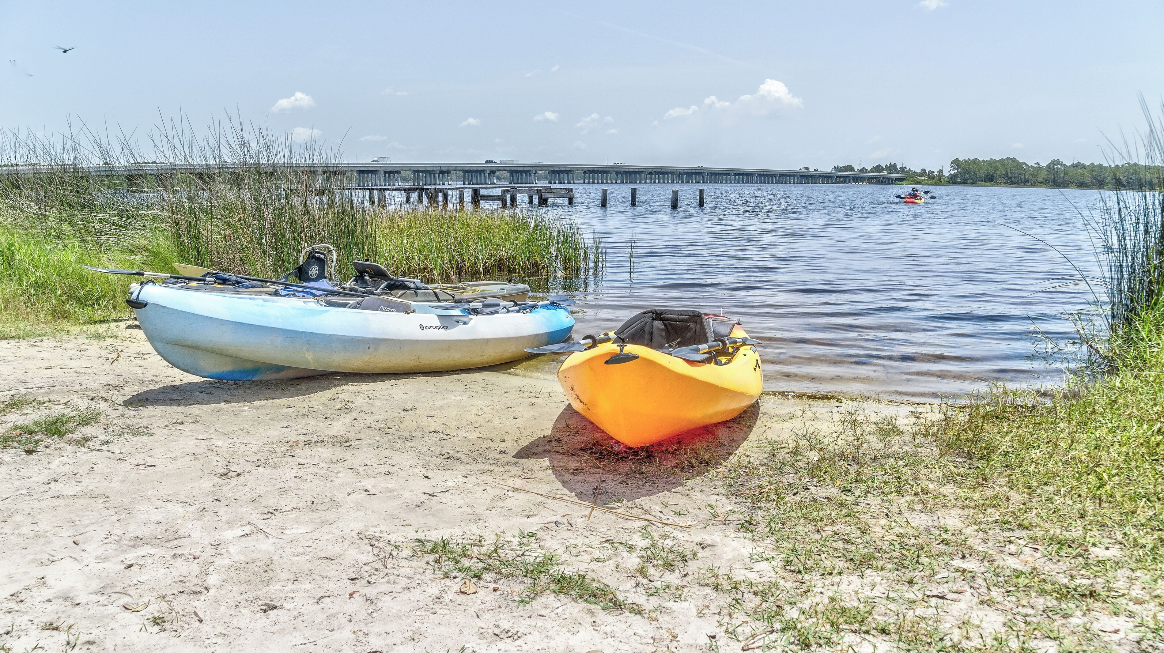 Two kayaks on a sandy shore with a bridge in the background.