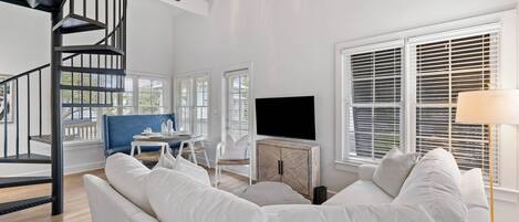 Una sala de estar moderna con un sofá blanco, un televisor sobre un mueble de madera, una silla azul y una escalera espiral.