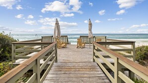 Un muelle de madera que conduce a sillas y sombrillas de playa, con vista al océano.