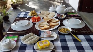 A table set with plates of toast, a bowl of fruit, a container of butter, and a teapot. - Venus Paradise (Sigiriya)