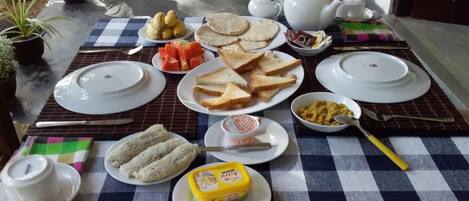 A table set with plates of toast, a bowl of fruit, a container of butter, and a teapot.