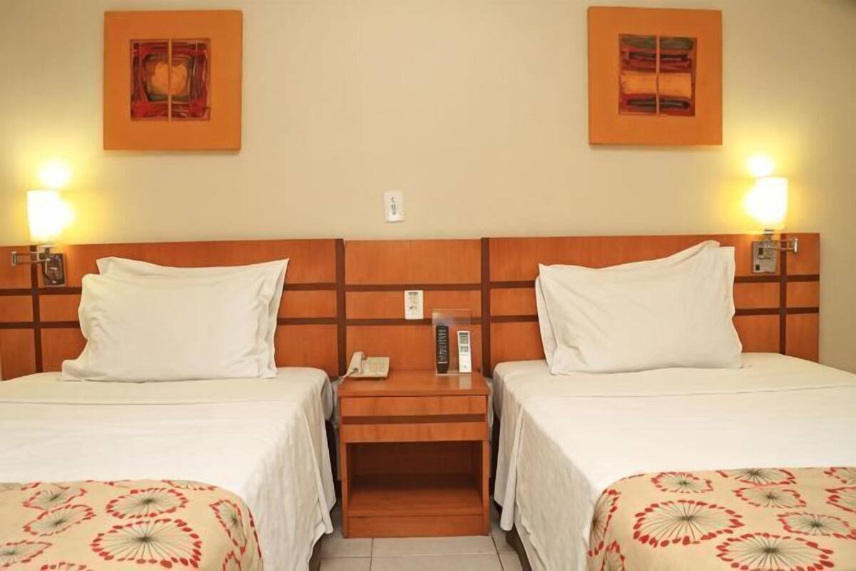 A hotel room with two beds, wooden headboards, bedside lamps, a phone, and artwork on the walls.