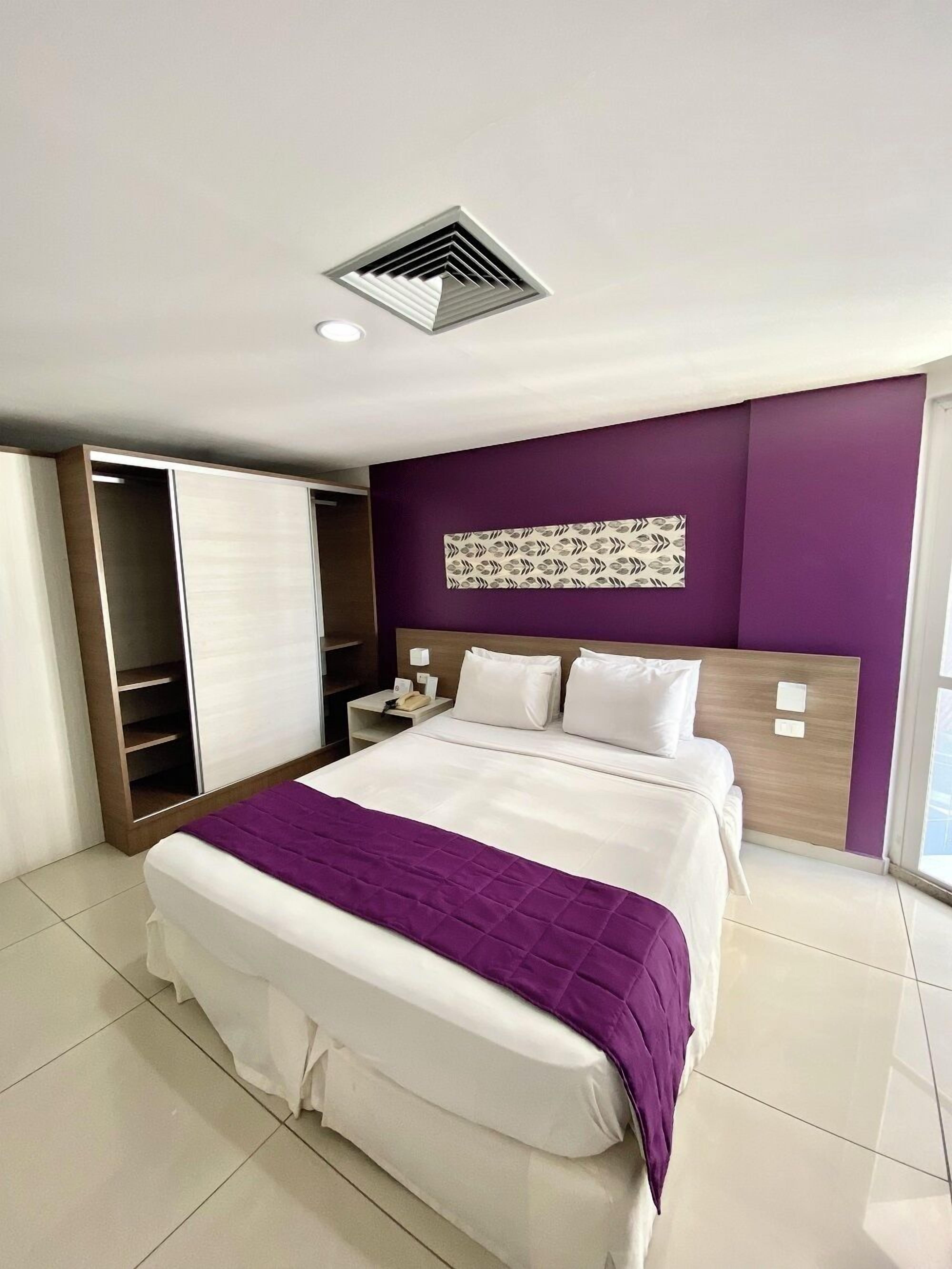 A modern hotel room with a bed, a wardrobe, a nightstand, and a decorative wall panel.