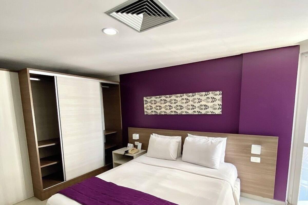 A modern hotel room with a bed, a wardrobe, a nightstand, and a decorative wall panel.