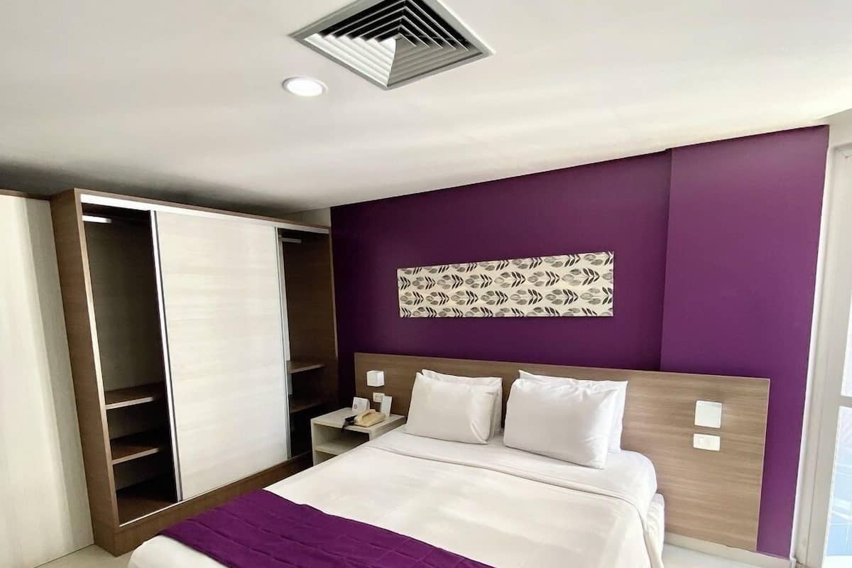 A modern hotel room with a bed, a wardrobe, a nightstand, and a decorative wall panel.
