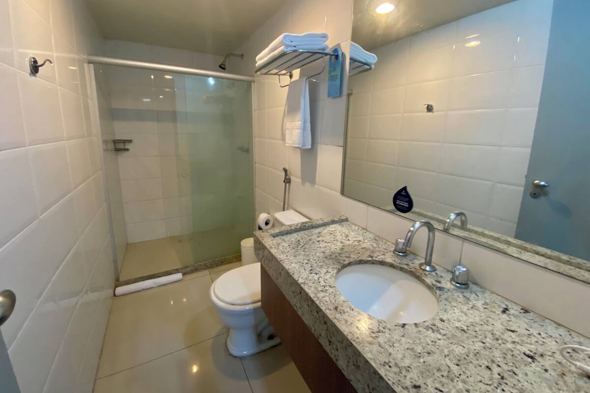 A bathroom with a glass-enclosed shower, a sink, a toilet, and a mirror.