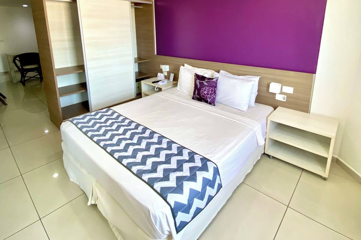 A hotel room with a bed, a nightstand, a wardrobe, and a purple accent wall.