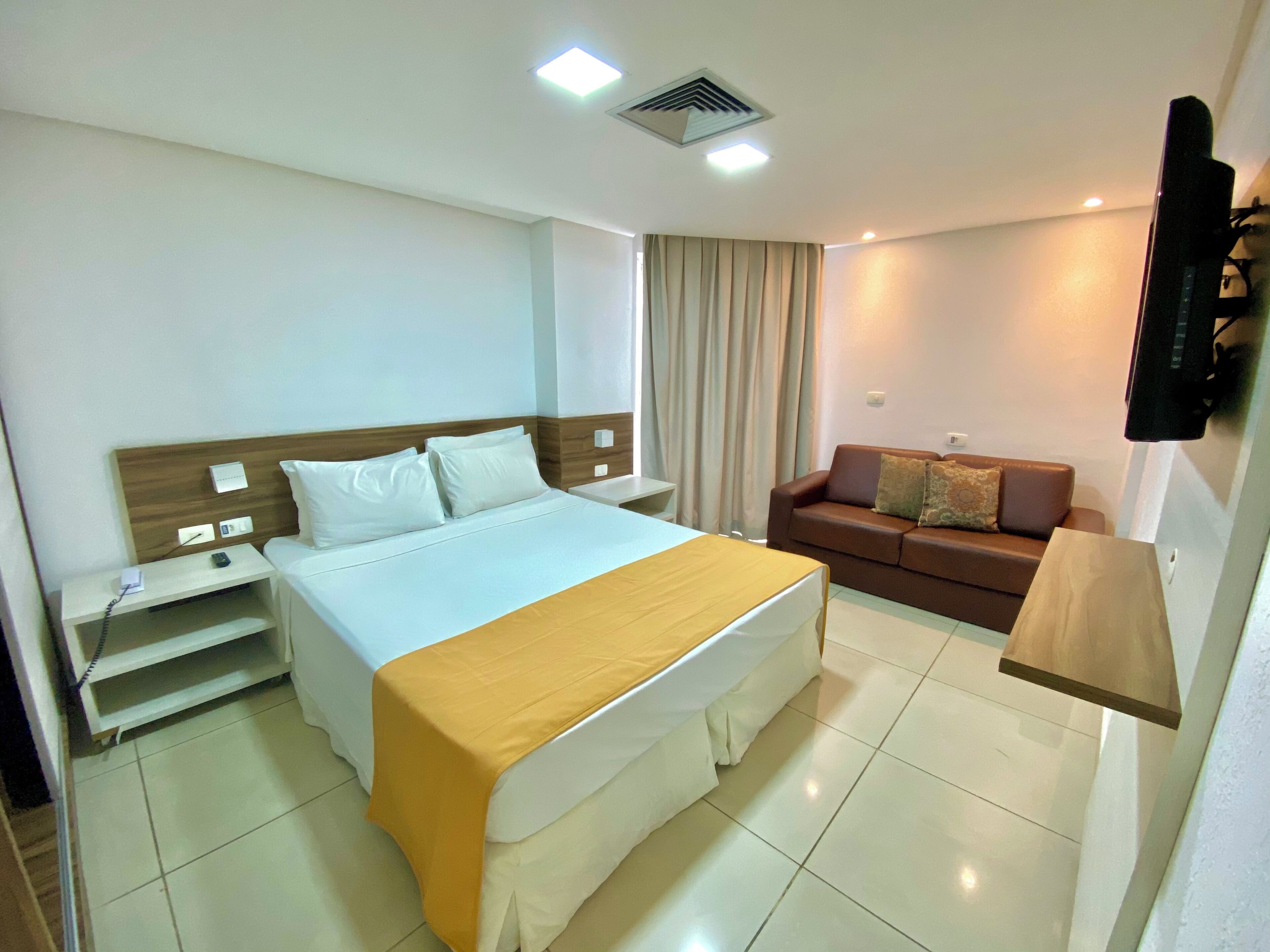 A hotel room with a bed, bedside table, TV, and a sofa.