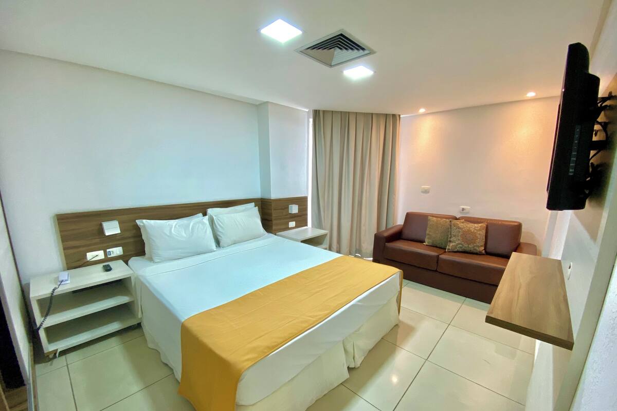 A hotel room with a bed, bedside table, TV, and a sofa.
