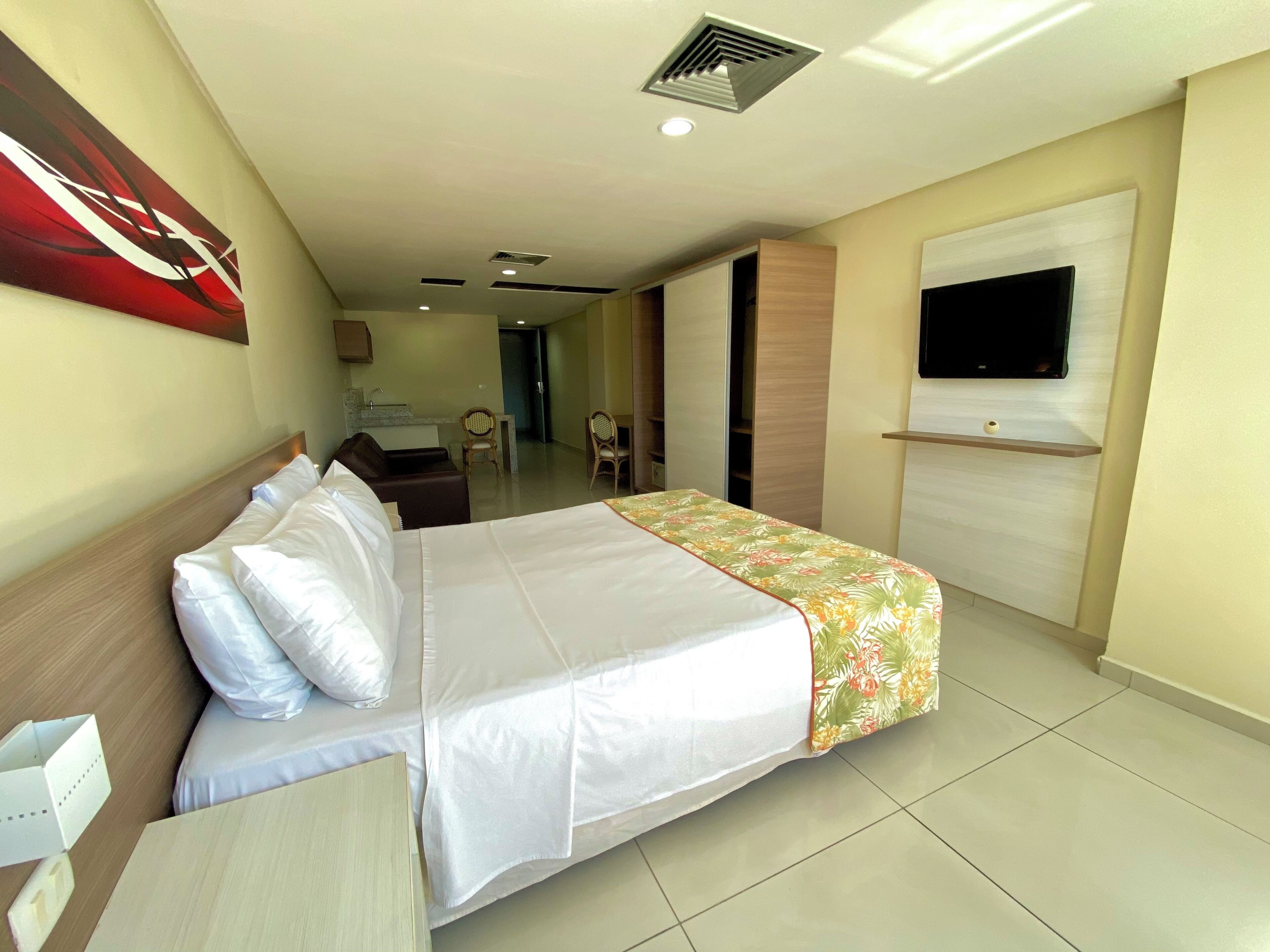A hotel room with a bed, a desk, a television, and a bathroom visible in the background.