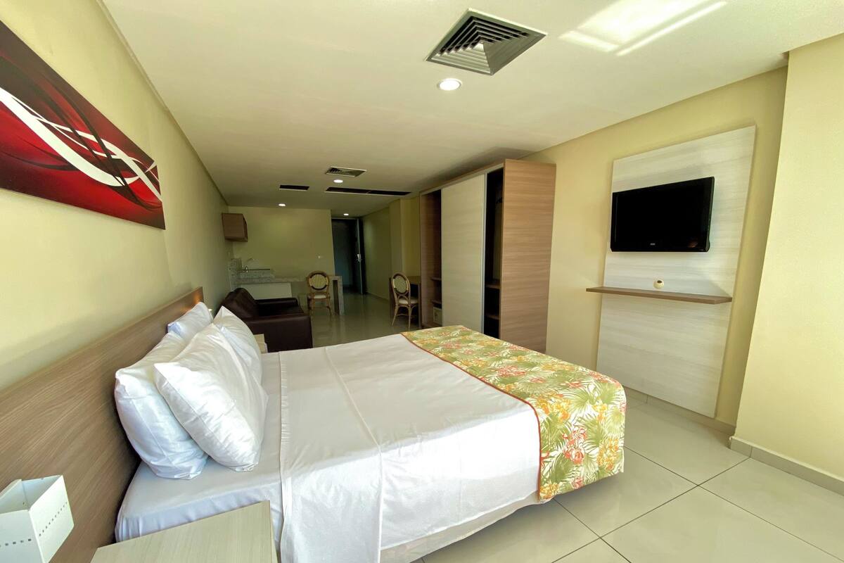 A hotel room with a bed, a desk, a television, and a bathroom visible in the background.