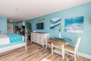Un dormitorio con cama, escritorio, silla, televisor y obras de arte en la pared.