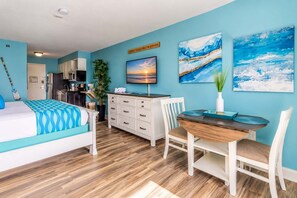A hotel room with a bed, a dining table, a TV, and artwork on the walls.