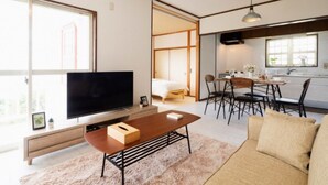 Ein modernes Wohnzimmer mit einem Flachbildfernseher, einem Couchtisch, einer Couch und einem Essbereich mit Tisch und Stühlen.