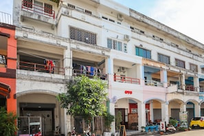 Un edificio de varios pisos con balcones, una tienda con un letrero y un coche amarillo estacionado.