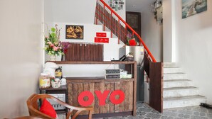 A reception desk with a sign reading "OYO" and a staircase with a red railing.