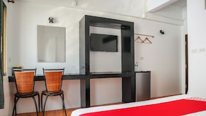 A hotel room with a bed, two chairs, a desk, a mirror, and a TV.