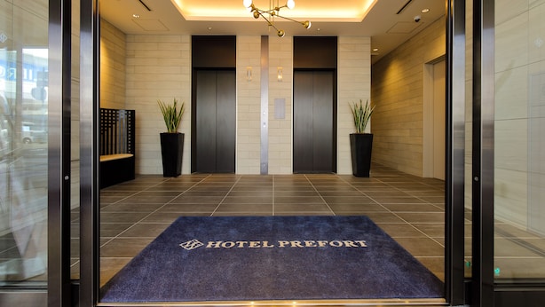 Een hotel lobby met een receptiebalie, twee liften en een blauw tapijt met de naam van het hotel.