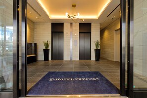 A hotel lobby with a reception desk, two elevators, and a blue carpet with the hotel name. - Hotel Prefort Nishiakashi (Akashi)