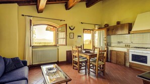A cozy living room with a sofa, a dining table with chairs, a kitchen with wooden cabinets, and a window with curtains. - Trebbiano-Panoramic apartment with swimming pool and vineyard (Reggello)